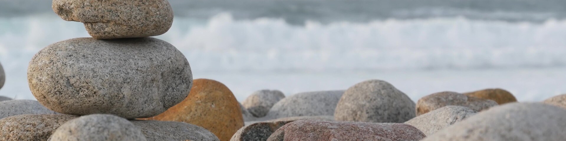 A stack of smooth, rounded stones on a pebbly beach with waves in the background.