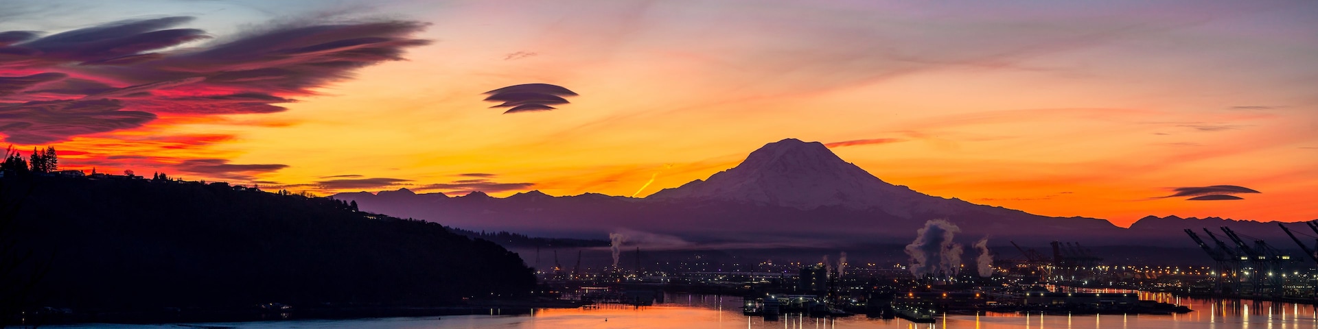 Ein Sonnenuntergang über einer Berglandschaft, im Vordergrund liegt eine Stadt.