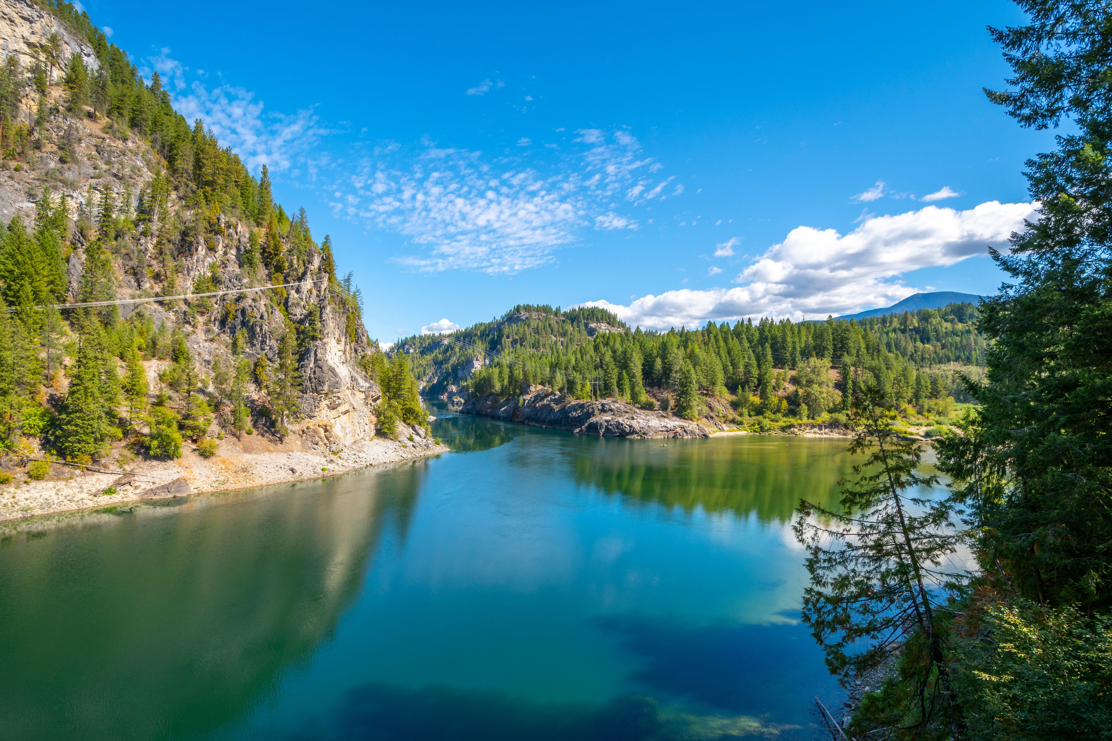 Un río serpentea a través de un paisaje montañoso con bosques densos y un cielo azul claro.