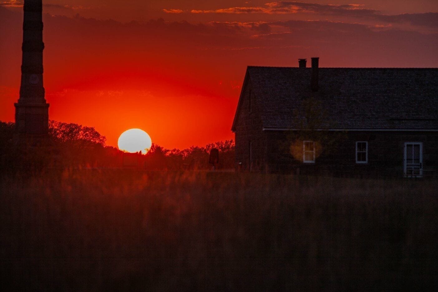 A sunset over a rural landscape with a prominent church steeple and a house.