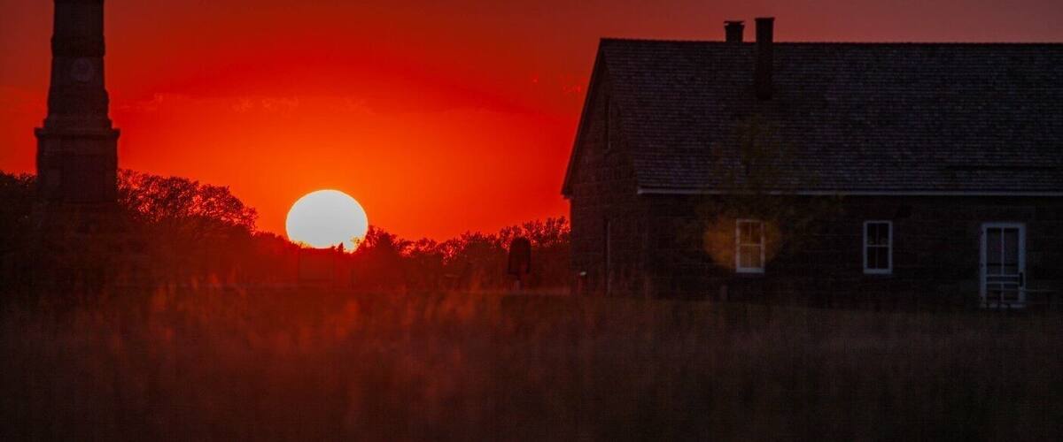 A sunset over a rural landscape with a prominent church steeple and a house.