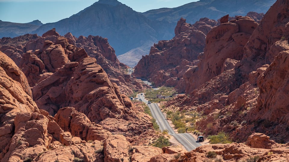 A winding road through a canyon with red rock formations and distant mountains.