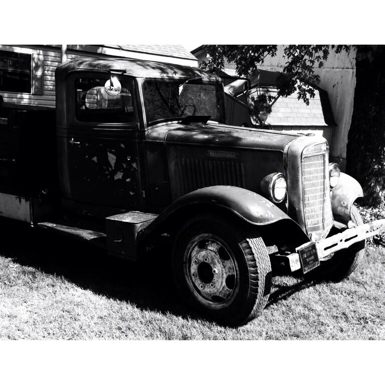 A vintage truck parked on a grassy area with a building in the background.