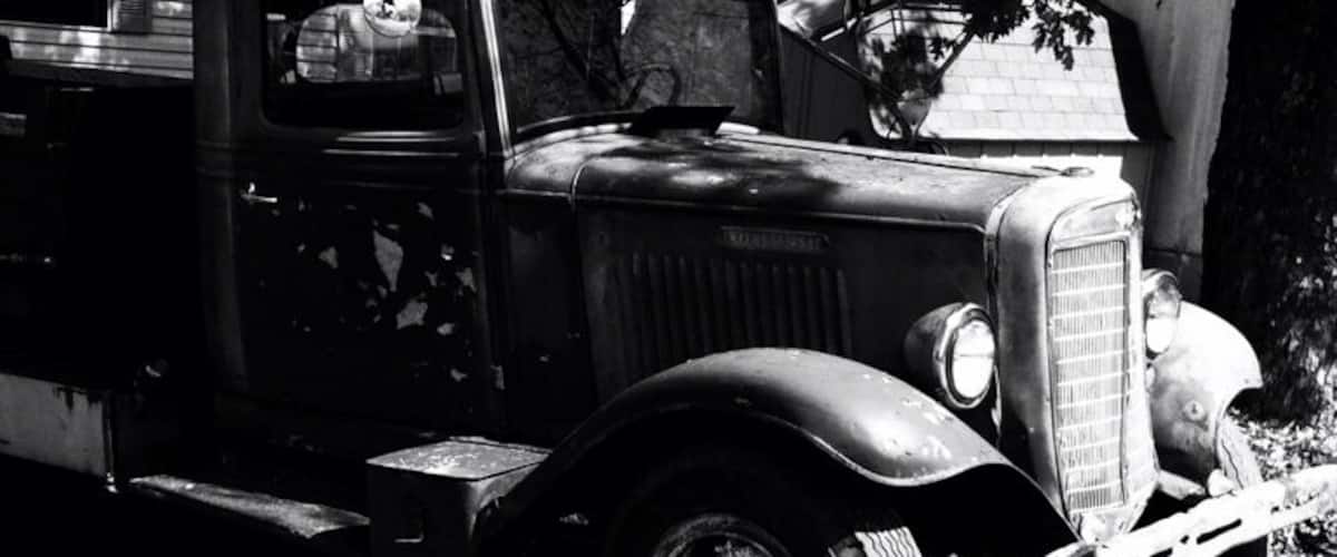 A vintage truck parked on a grassy area with a building in the background.