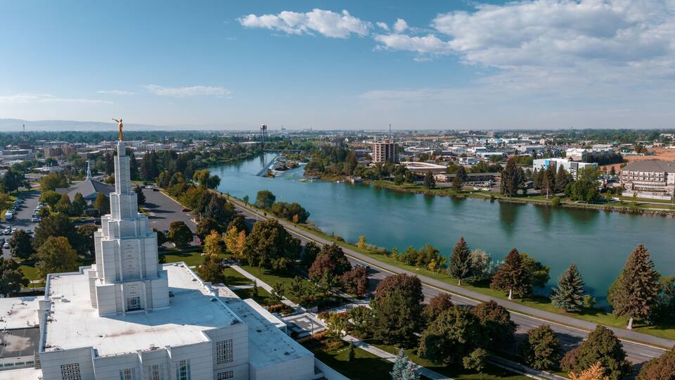 A river with a bridge, a statue, and a cityscape with buildings and trees.
