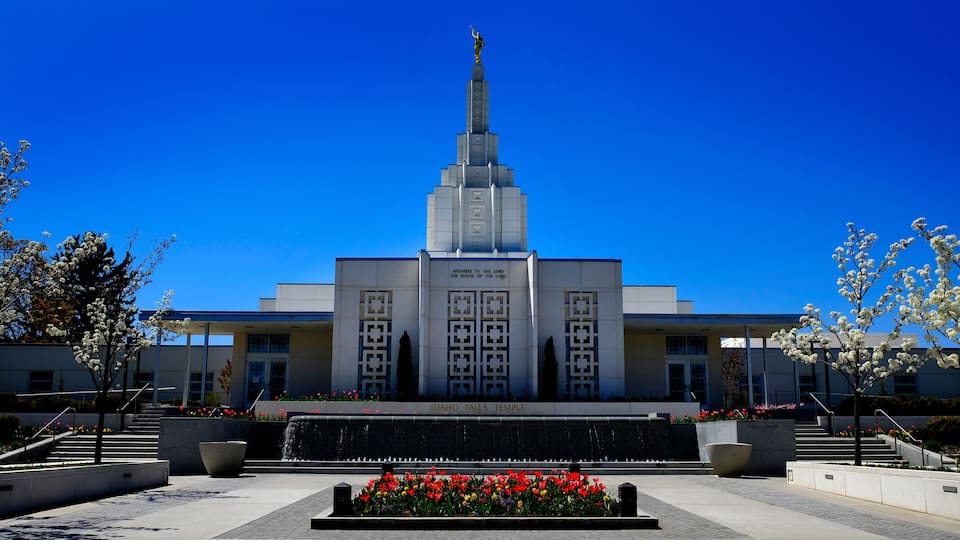 The Idaho Falls Temple with a spire, a fountain, and a garden with flowers.