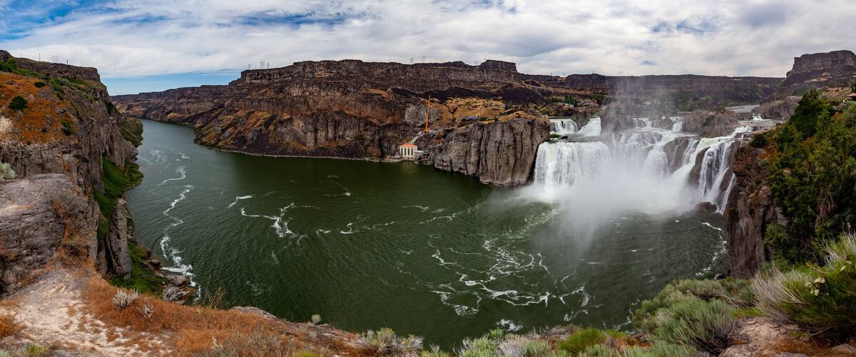A large waterfall cascading down a steep cliff into a river surrounded by rocky terrain and sparse vegetation.