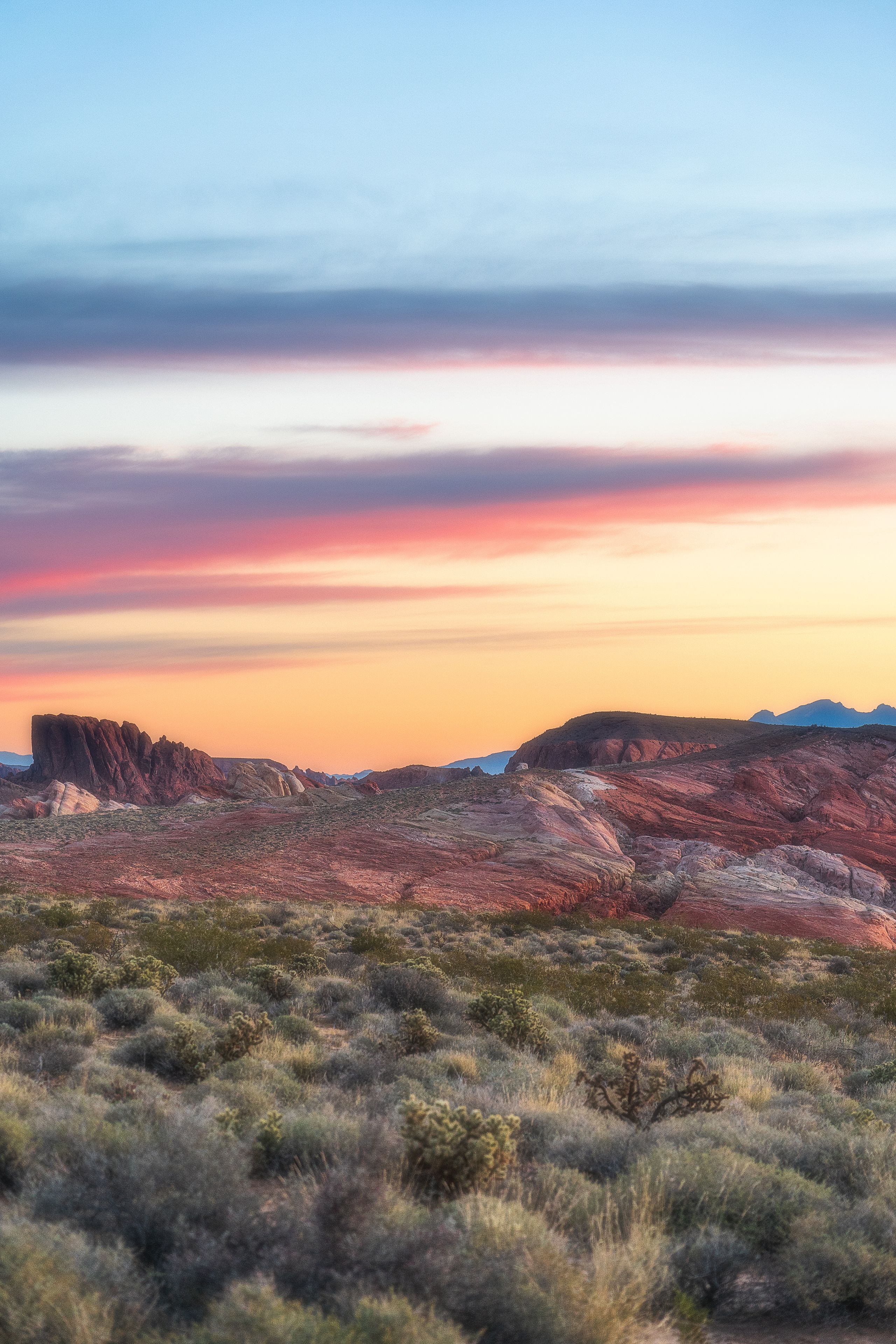 A desert landscape with rocky formations and sparse vegetation during sunset.