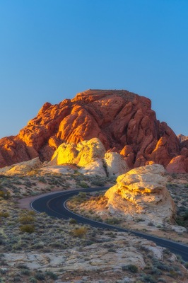 Una carretera sinuosa atraviesa un paisaje desértico con formaciones rocosas rojas.