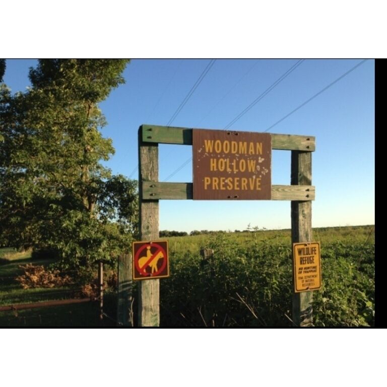 A sign for Woodman Hollow Preserve with a no wildlife refuge and no trespassing symbol.