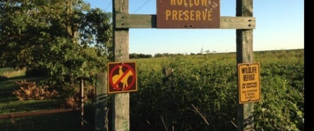 A sign for Woodman Hollow Preserve with a no wildlife refuge and no trespassing symbol.