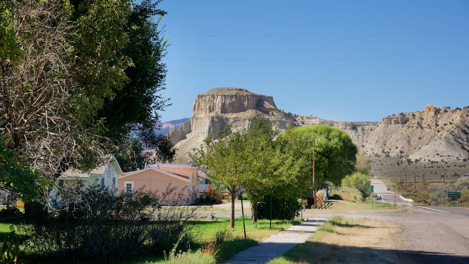 A rural landscape with a prominent rock formation in the background, surrounded by greenery and a few houses.
