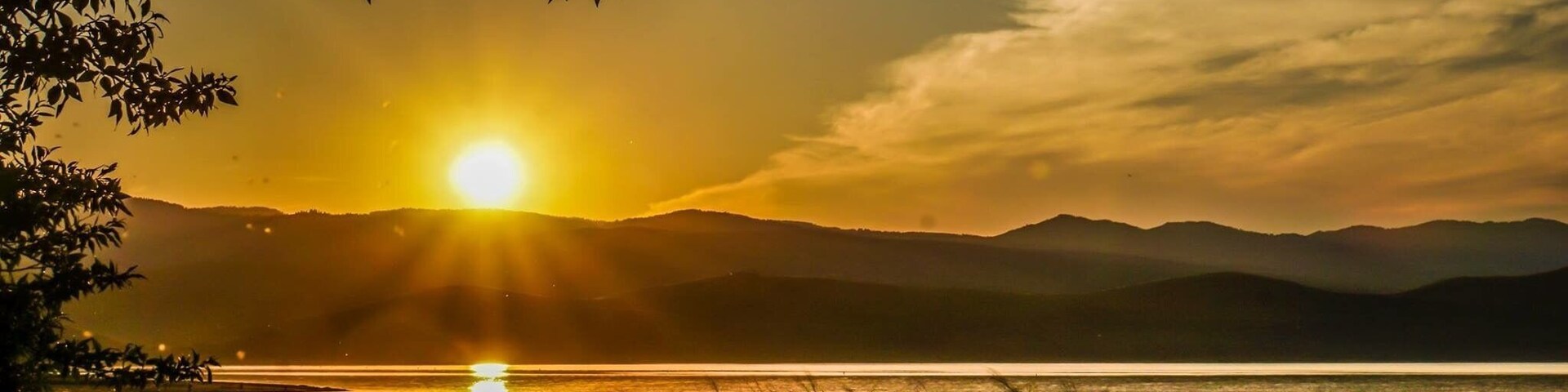 Un atardecer sobre un lago con montañas al fondo.