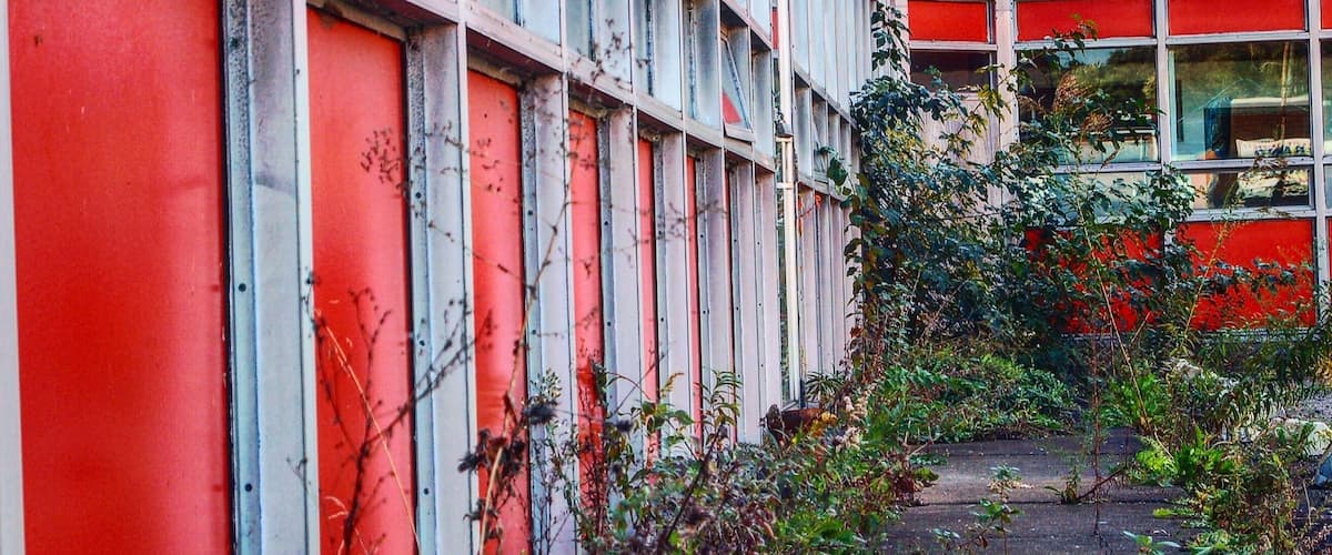 A red building with multiple windows and overgrown vegetation.