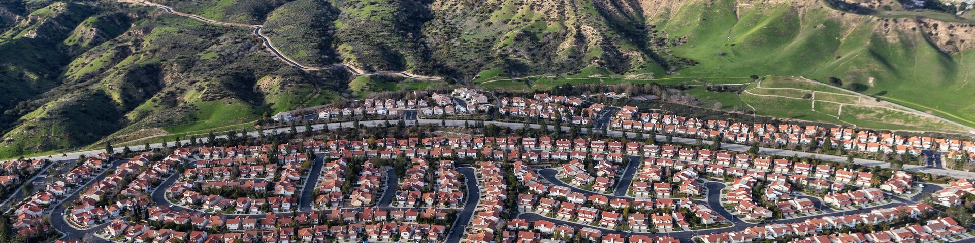 Una zona residencial con calles sinuosas y casas, rodeada de colinas y montañas verdes.