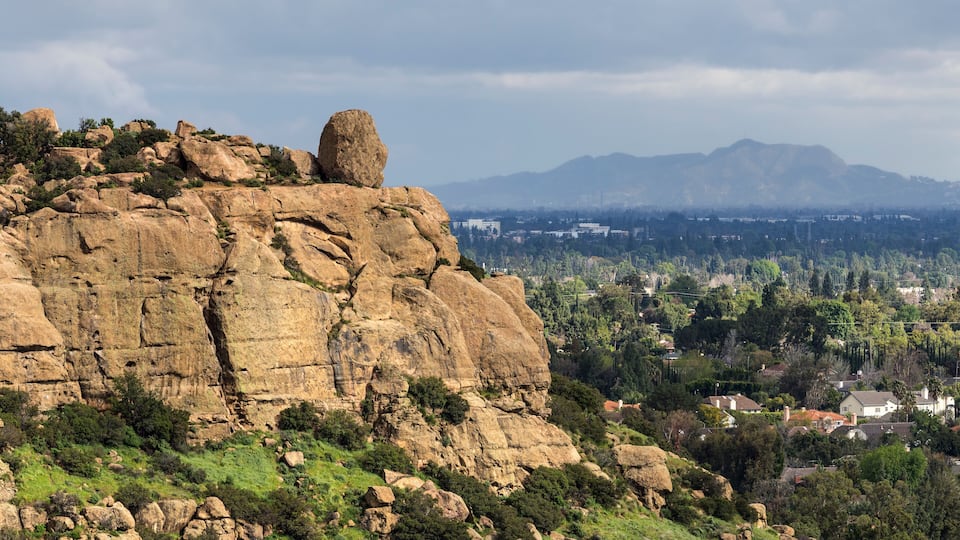 A rocky hill with a prominent boulder, a town in the valley below, and distant mountains.