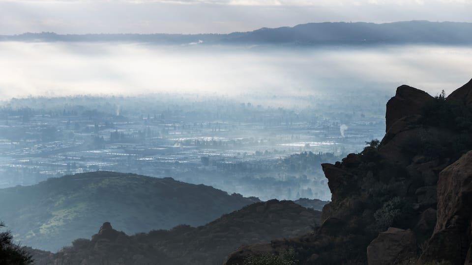 A misty valley with a cityscape in the distance, surrounded by rocky terrain.