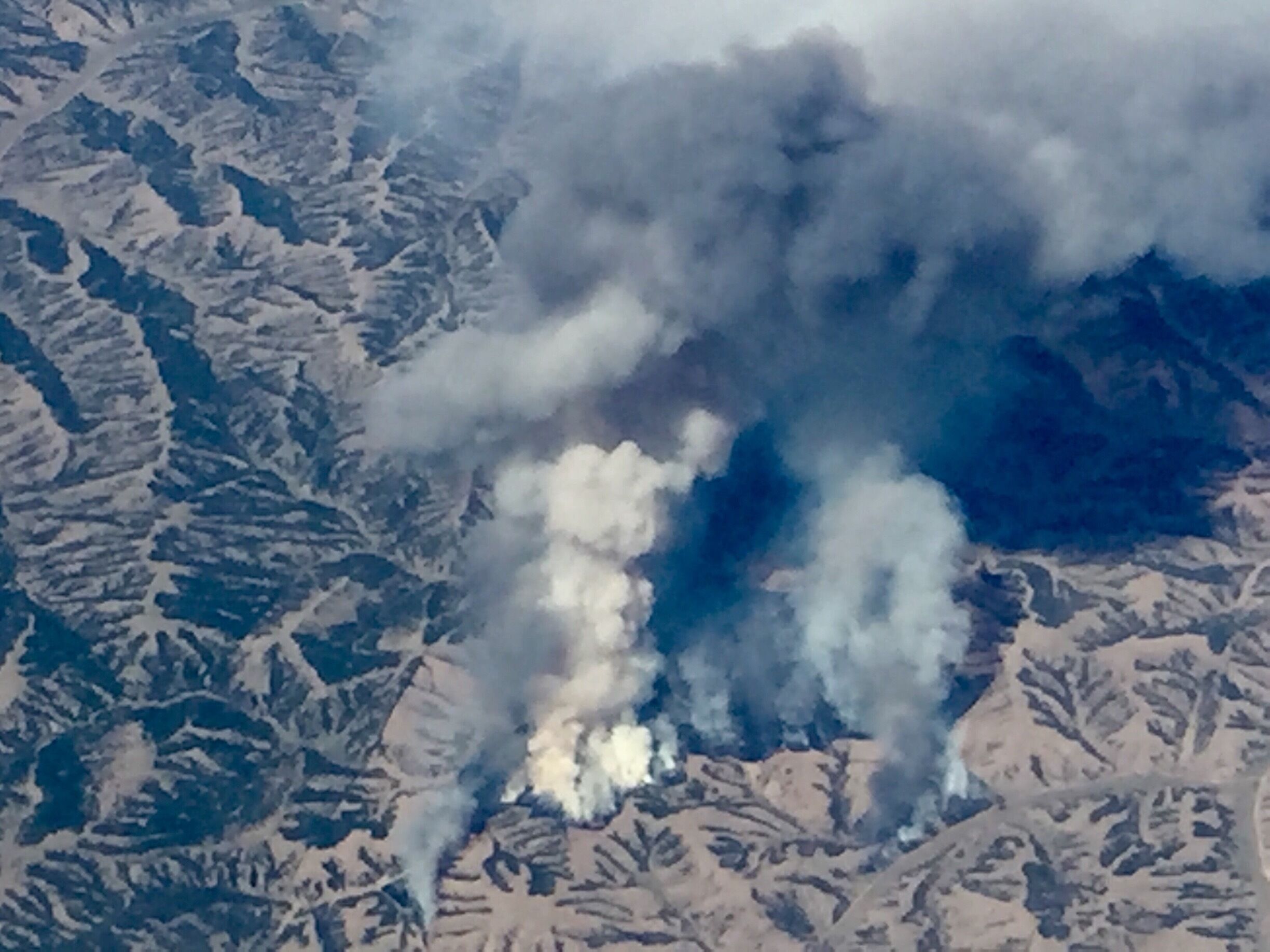 A mountainous landscape with a visible smoke plume.