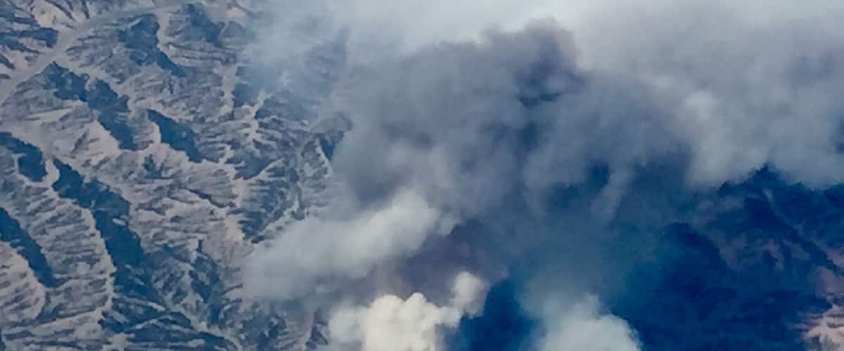 A mountainous landscape with a visible smoke plume.