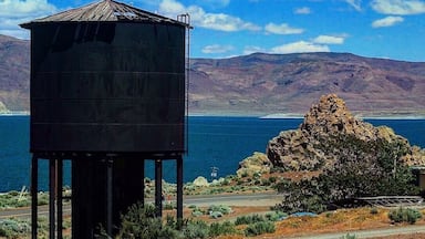 Uma torre de água, uma colina rochosa e um corpo de água com montanhas ao fundo.