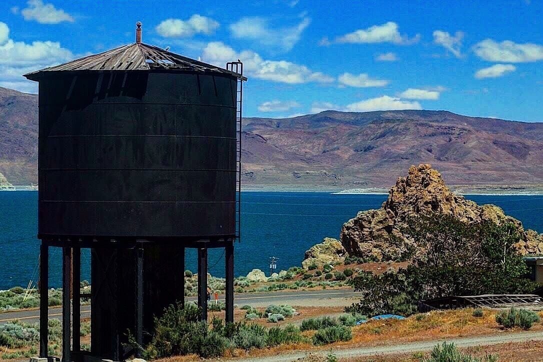 A water tower, a rocky hill, and a body of water with mountains in the background.