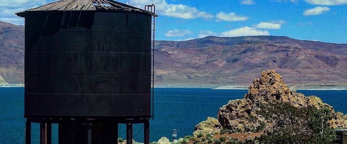 A water tower, a rocky hill, and a body of water with mountains in the background.
