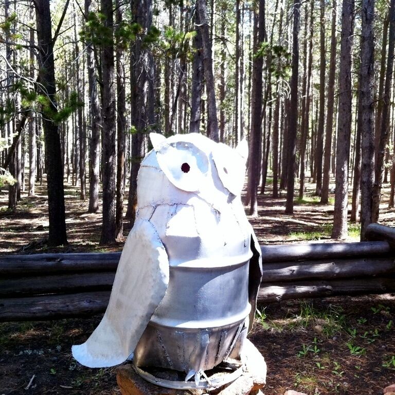 A metal owl sculpture in a forest.
