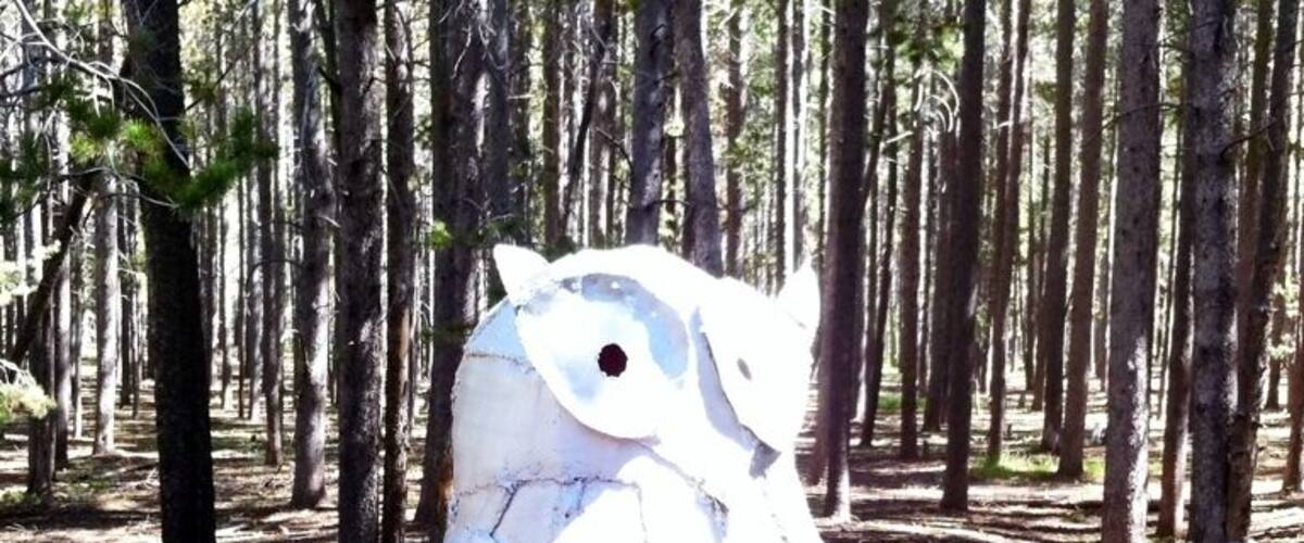 A metal owl sculpture in a forest.