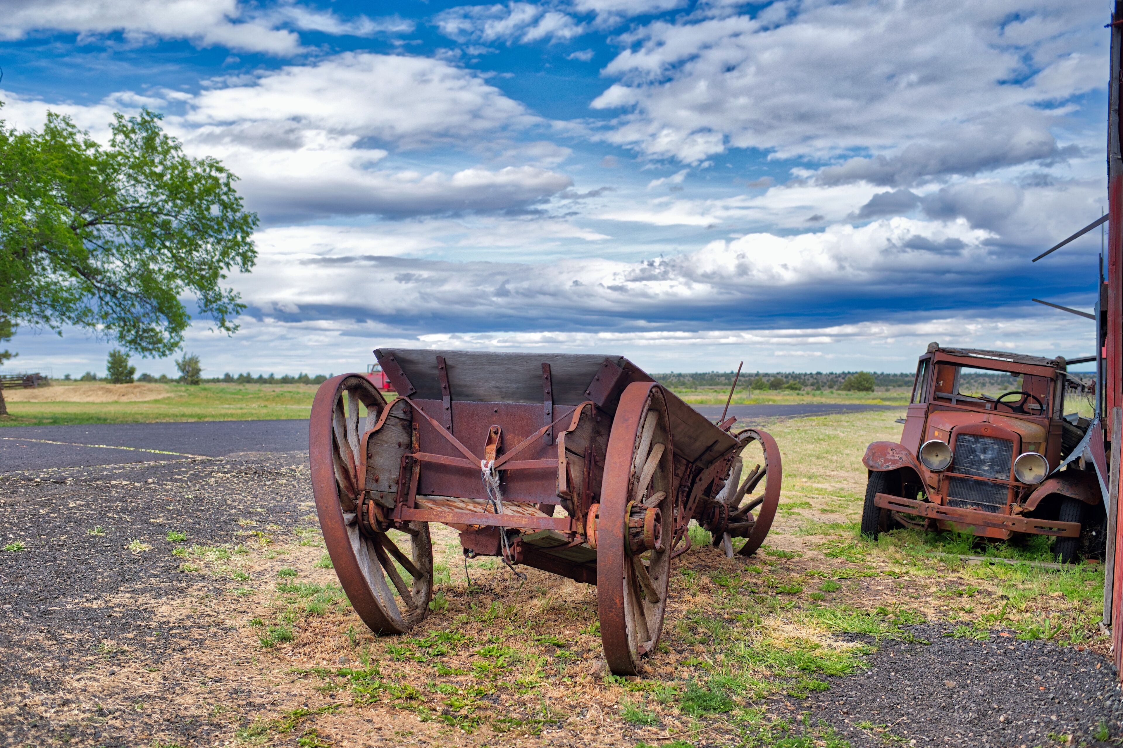 An old rusty tractor and a wooden cart in a rural field with a cloudy sky.