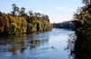 A calm river with a kayaker, surrounded by autumn foliage and a bridge in the background.