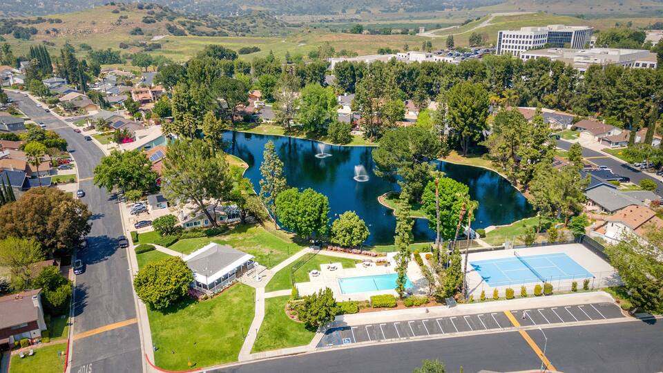 A residential area with a large pond, tennis courts, and a parking lot.