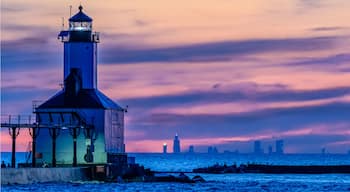 A lighthouse at sunset with a city skyline in the background.