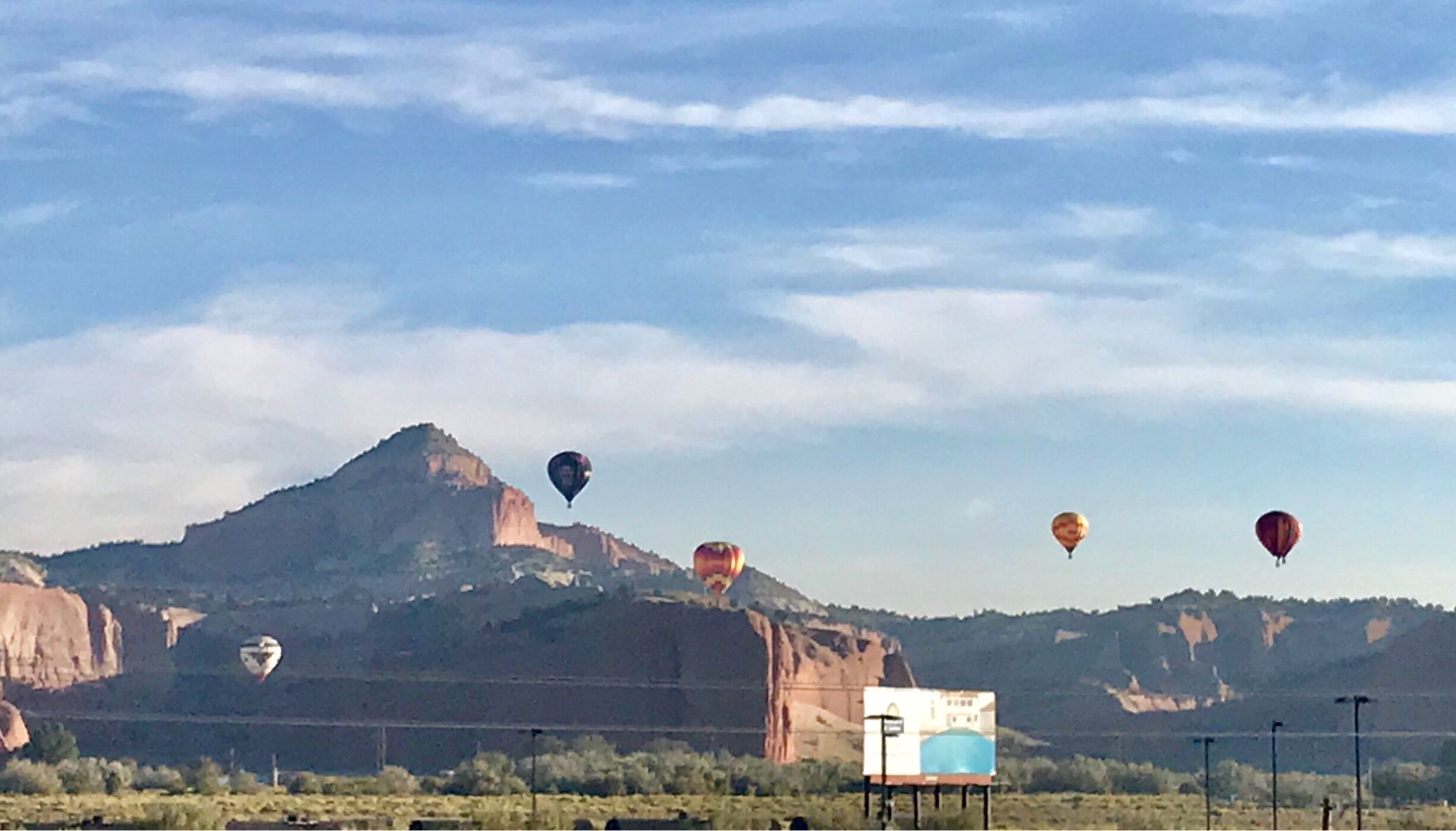 A landscape with a prominent mountain and several hot air balloons in the sky.