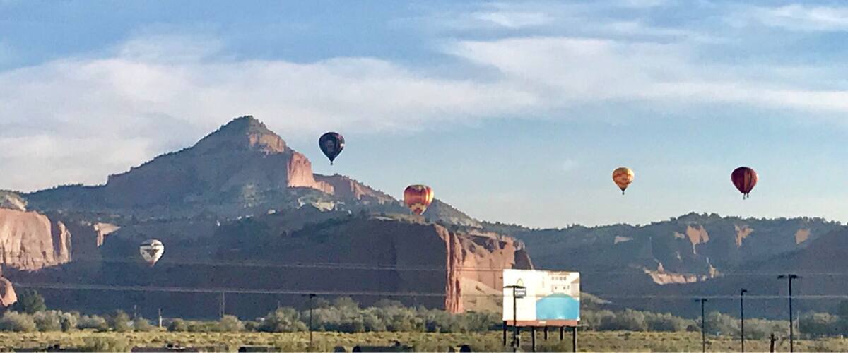 A landscape with a prominent mountain and several hot air balloons in the sky.