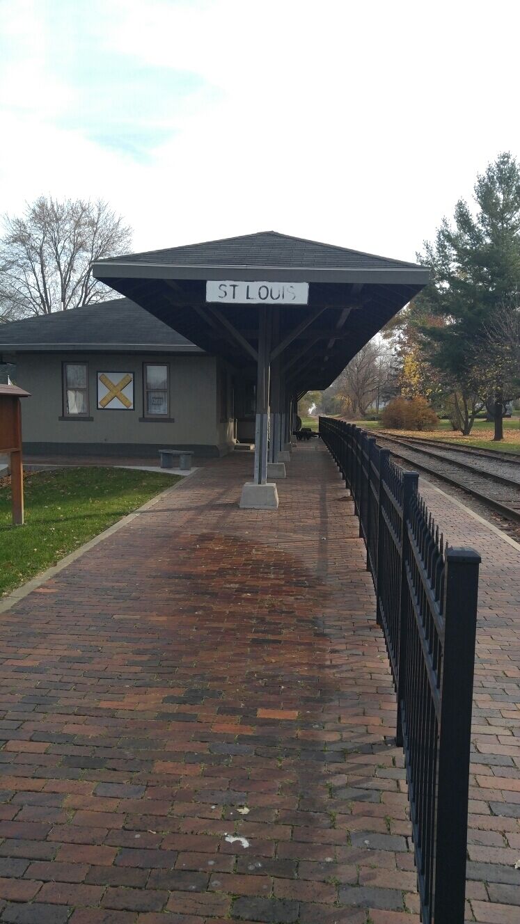 A covered train station platform with a sign reading "ST LOUIS" and a yellow 'X' symbol on the wall.