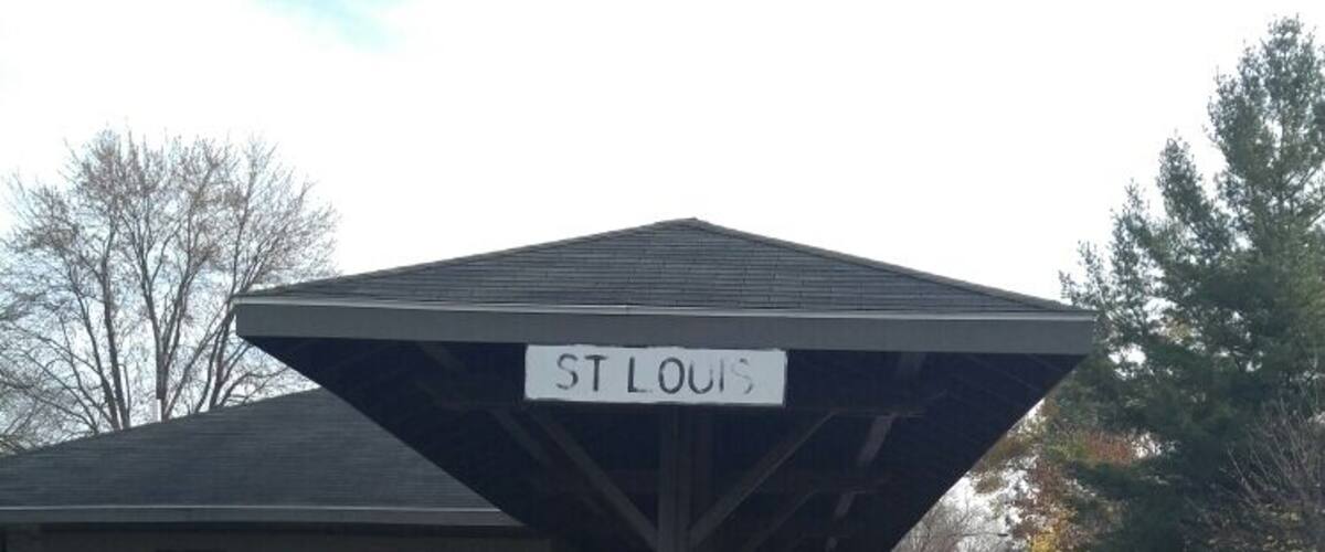 A covered train station platform with a sign reading "ST LOUIS" and a yellow 'X' symbol on the wall.