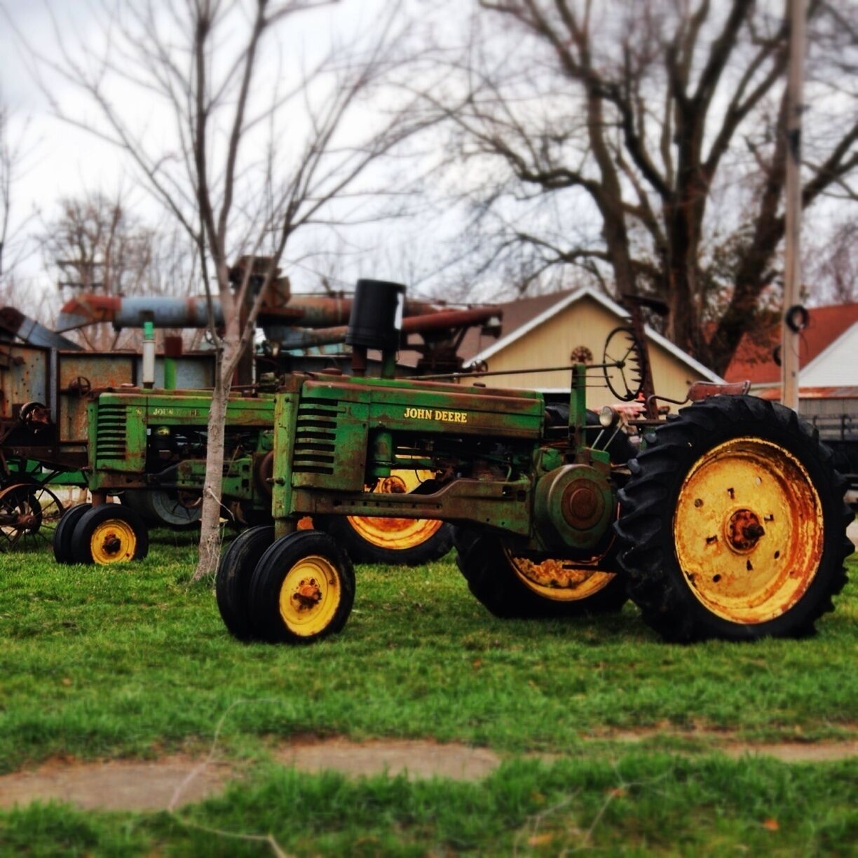A John Deere tractor on a grassy field with trees and a building in the background.