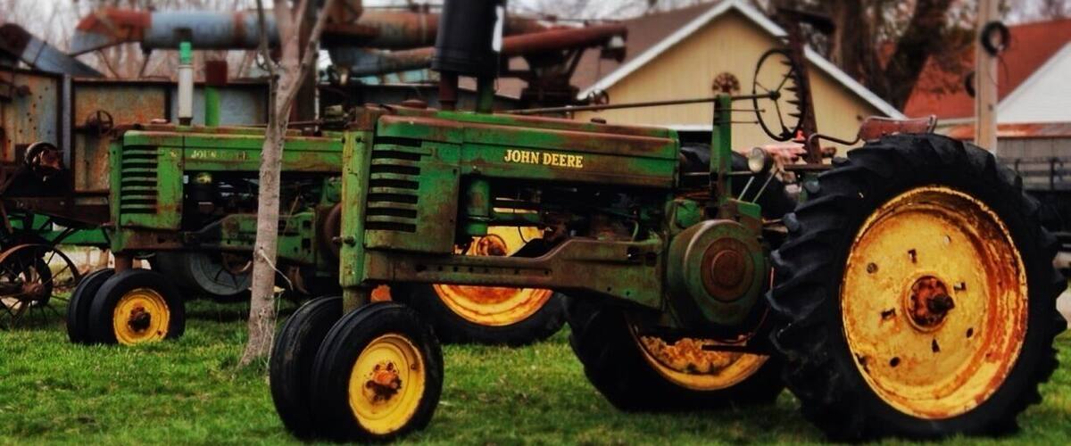 A John Deere tractor on a grassy field with trees and a building in the background.