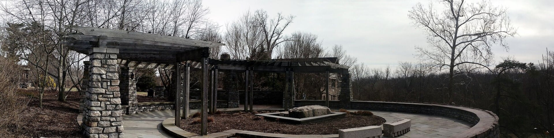A stone gazebo with a circular brick patio and a stone wall.
