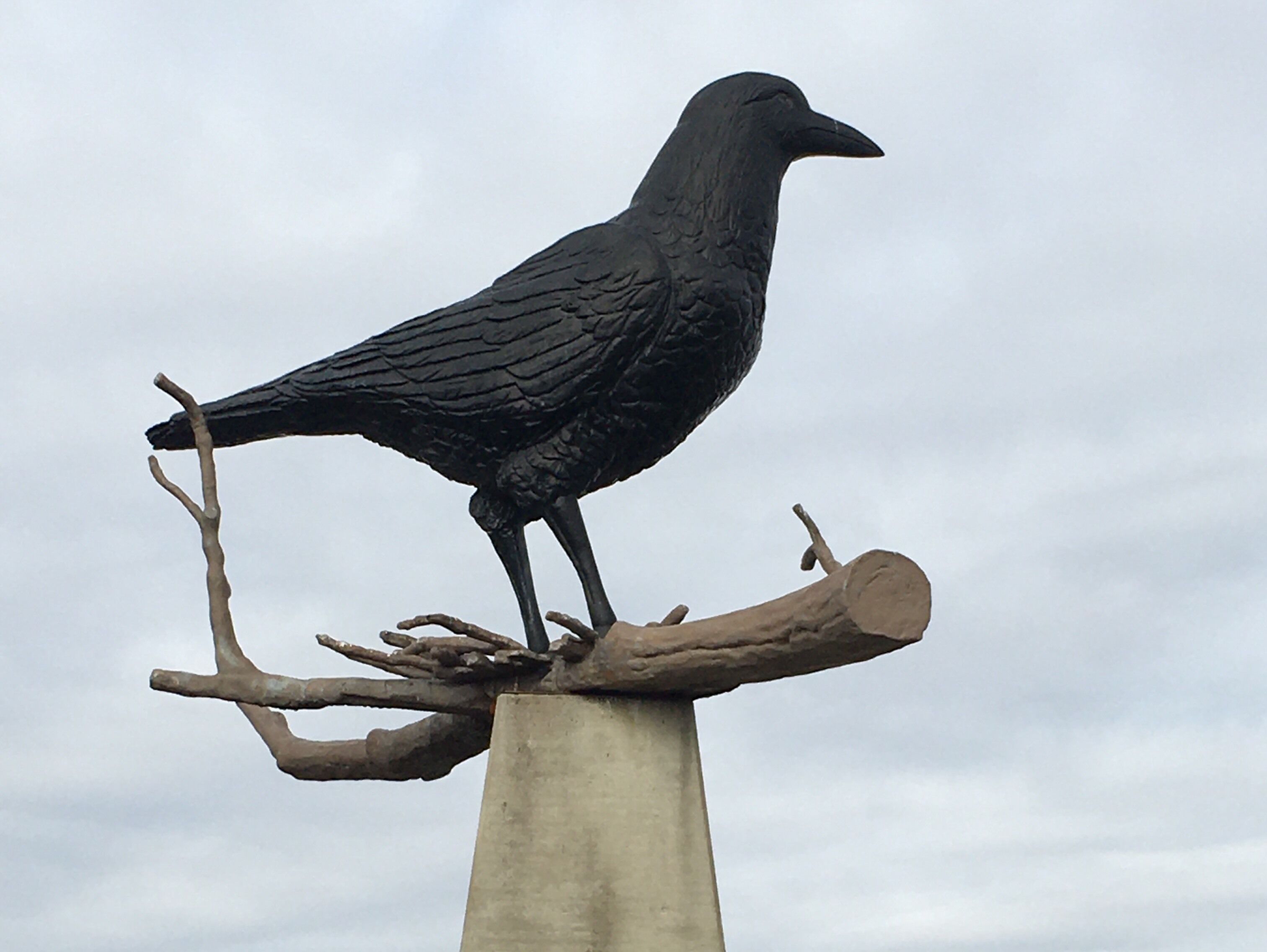 A black bird statue perched on a branch atop a concrete post.