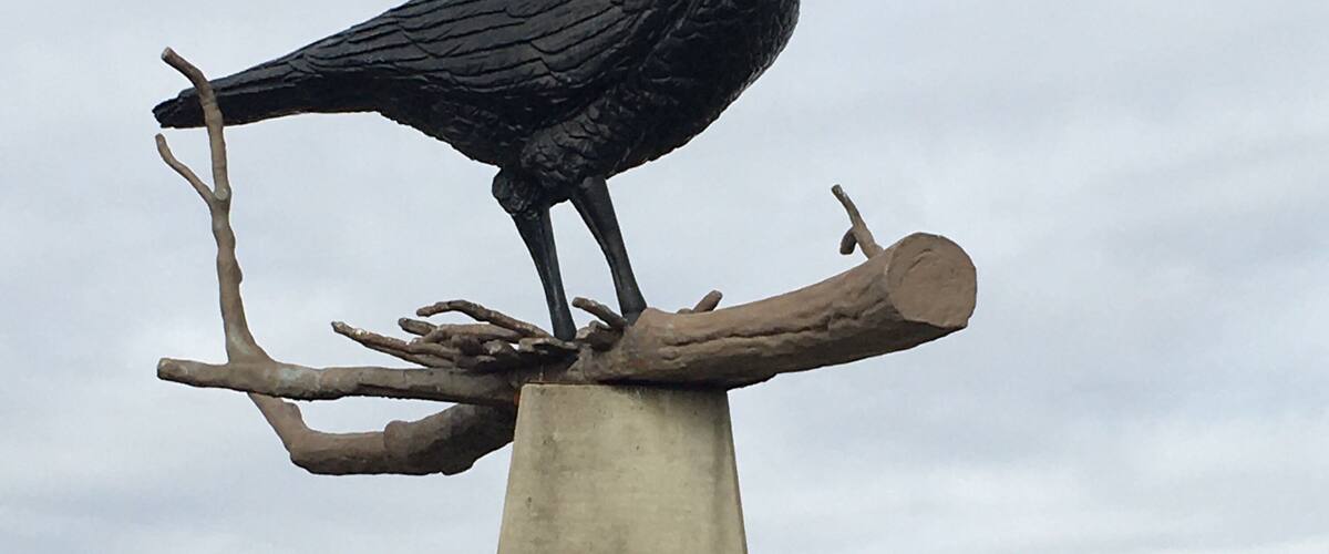 A black bird statue perched on a branch atop a concrete post.