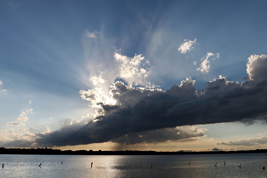 Un coucher de soleil sur un lac paisible, avec quelques nuages épars et les silhouettes lointaines de la rive.