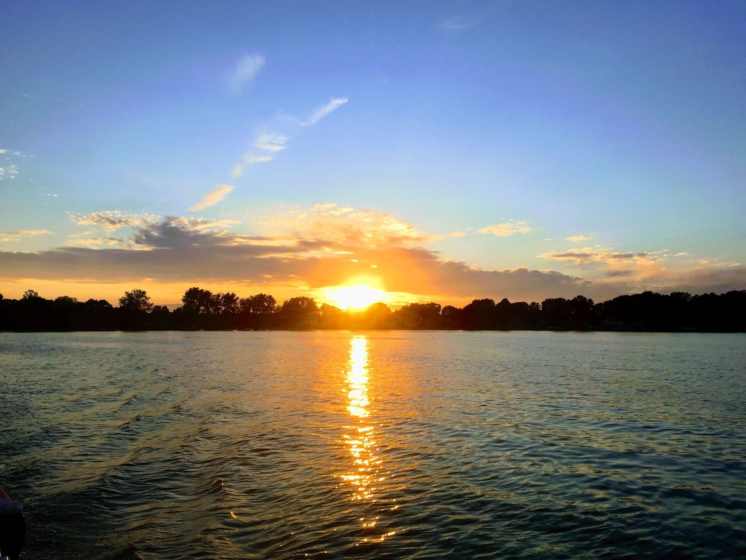 A sunset over a calm lake with a silhouette of trees and a clear sky.