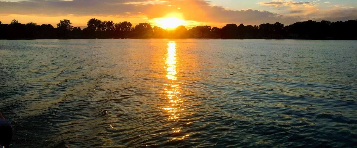 A sunset over a calm lake with a silhouette of trees and a clear sky.