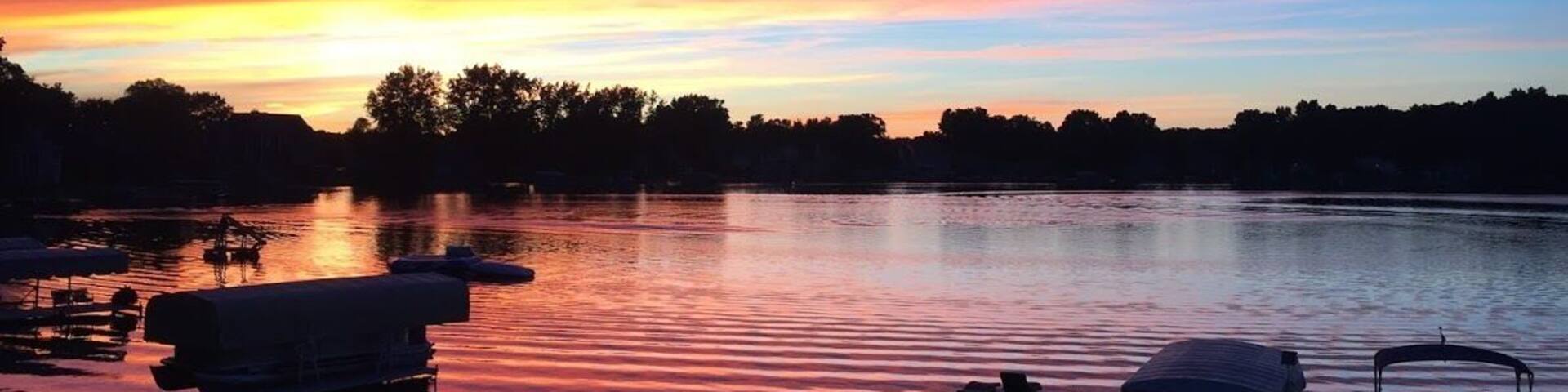 A sunset over a calm lake with boats docked at the pier.