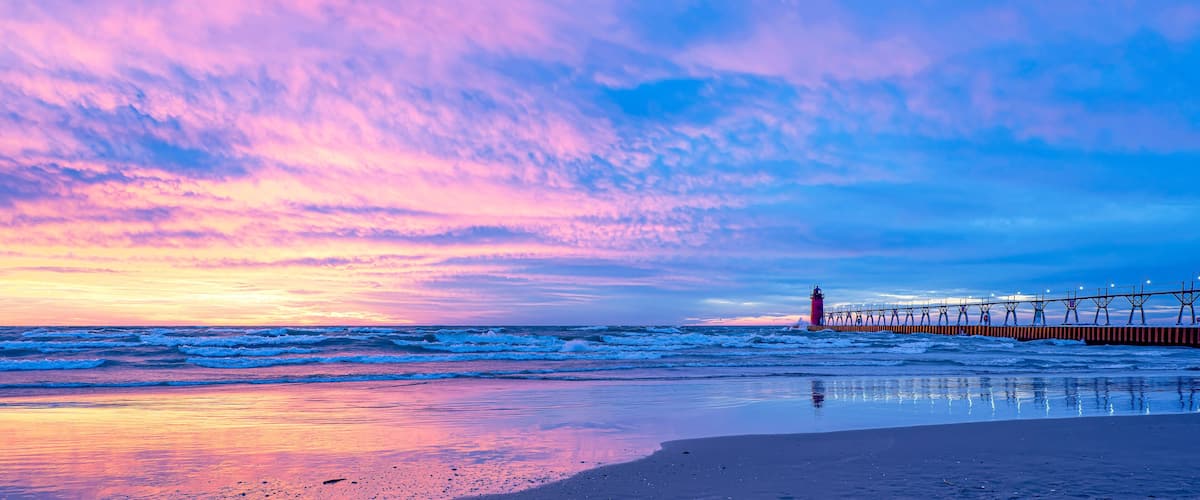 A beach with waves, a pier, and a lighthouse.