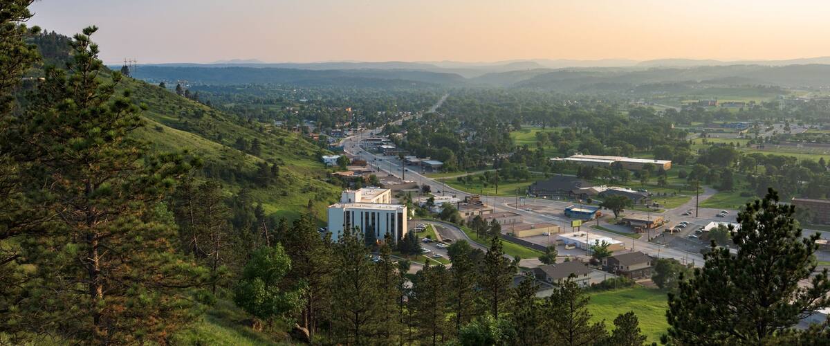 A town nestled in a valley with a prominent white building, surrounded by hills and greenery.