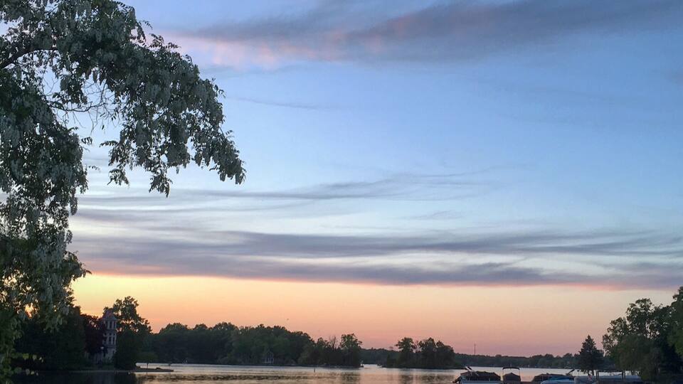 A calm lake at sunset with boats and trees reflecting the sky.