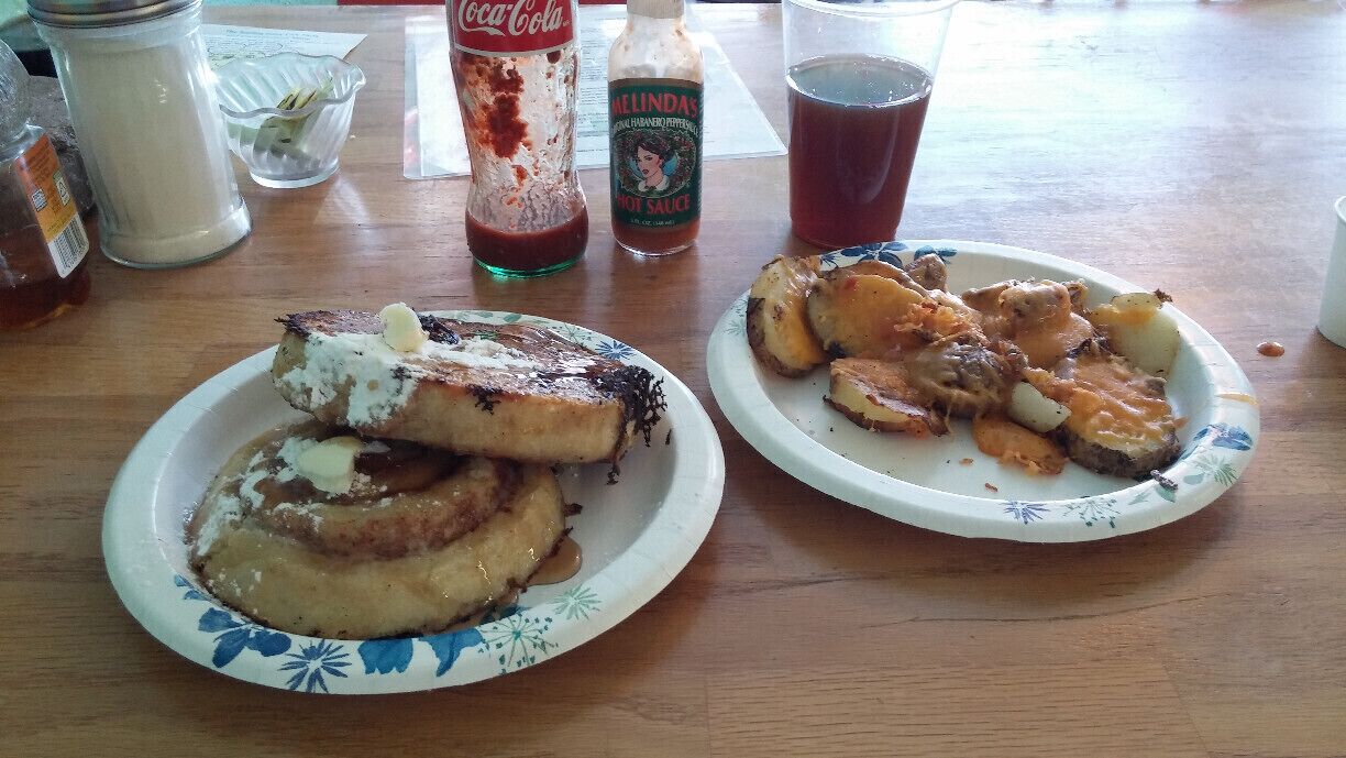 French toast made with a halved and griddled cinnamon roll with a side of potatoes and cheese and a dash of house made hot sauce.