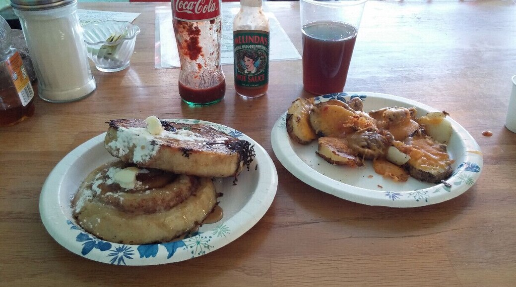 French toast made with a halved and griddled cinnamon roll with a side of potatoes and cheese and a dash of house made hot sauce.